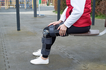 Woman wearing knee brace or orthosis after leg surgery, walking in the park