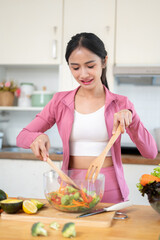 An attractive and slim Asian woman in sportswear is making a healthy salad bowl in the kitchen.