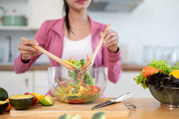A woman in sportswear is mixing her healthy fresh salad in a mixing bowl, cooking in the kitchen