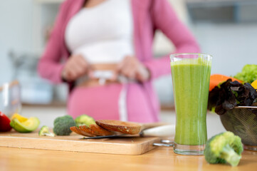Close-up image of a glass of a healthy green smoothie and fresh vegetables on a table in the kitchen
