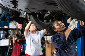 Black auto mechanic woman working in auto repair shop with Asian technician man background