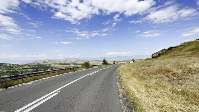 POV asphalt road, dry grass meadows, rocks, beautiful blue sky with clouds