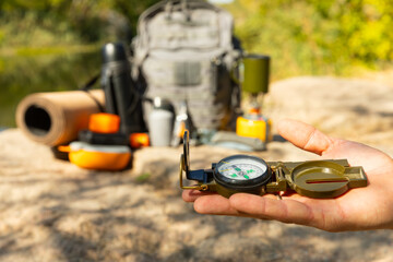 Man traveler holding a compass in her hand in the summer mountains at dawn.Tourist in the mountains with a compass against the backdrop of nature.The concept of tourism,sports and active recreation