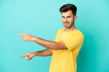 Young caucasian handsome man isolated on blue background pointing finger to the side and presenting a product