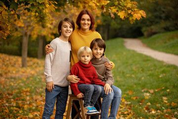 Fototapeta premium Cute blond toddler child and sibling brothers, standing next to autumn wooden stand with decoration, apples, leaves, mug, hedgehock in the park