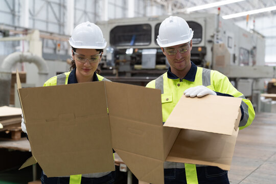 Male and female factory worker inspecting quality of cardboard in corrugated carton boxes warehouse storage. Group of factory worker checking cardboard corrugated carton boxes in factory