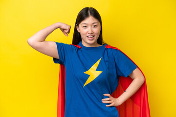 Young Chinese woman isolated on yellow background in superhero costume and doing strong gesture