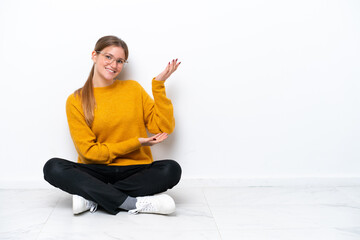 Young caucasian woman sitting on the floor isolated on white background extending hands to the side for inviting to come