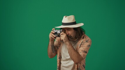 Man tourist in casual clothing and straw hat taking photos on old film camera. Isolated on green background.