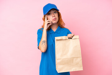 Young caucasian woman taking a bag of takeaway food isolated on pink background thinking an idea