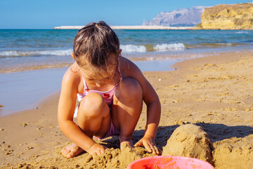Portrait of amazing little girl sister wearing swimsuit, sitting on beach seashore, playing with...