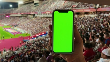 A man watches football at the stadium, holds a phone with a green screen in his hands. Makes bets on sports. - Powered by Adobe