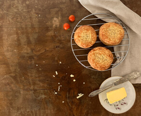 Three spelt cheese scones on a round wire rack to the side of an old wooden table