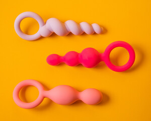 A set of three silicone anal beads of various shapes and sizes on an orange background.