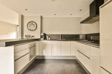 a kitchen with black counter tops and white cupboards on the wall behind it is a large clock in the corner
