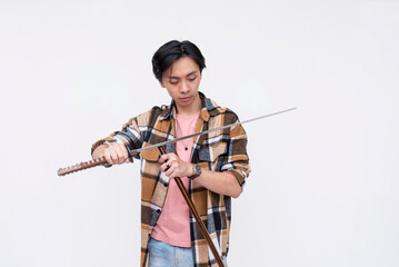 A young asian man puts back a ceremonial katana into its sheath. A sword enthusiast feeling like a samurai warrior. Isolated on a white background.