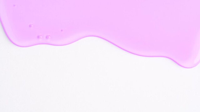 Liquid light purple drops of cosmetics product with bubbles flowing on the white surface. Macro shot of shower gel of lavender color  dripping on the wall with copy space. Close-up. Slow Motion