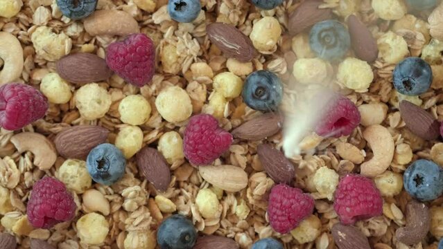 Pour milk on crunchy granola cereals. Morning eating with flakes, raspberries, blueberries, nuts, oatmeal. Healthy breakfast concept, Healthy food, clean eating, closeup, rotation background