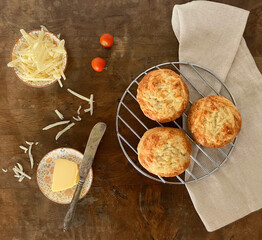 Overhead view of spelt flour cheese scones on an old wooden table with cheese, butter, an old knife and beige cloth