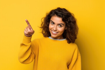A 17 years old girl on a yellow background gesticulates with her index finger, copy space - obrazy, fototapety, plakaty