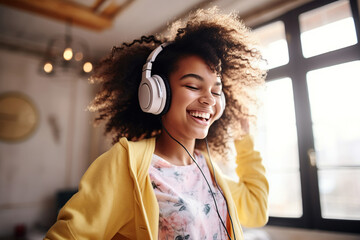 Happy funny gen z hipster African American teen girl wearing headphones dancing at home, listening...