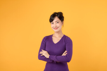 Unleash the power of confidence as a young Asian woman in her 30s, donning purple shirt, exhibits crossed arm sign gesture on yellow background.