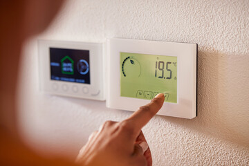 Ethnic woman adjusting smart thermostat control on wall