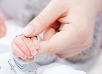 Fototapeta na wymiar Newborn baby touching his mother hand. Mother uses her hand to hold her baby's tiny hand to make him feeling her love, warm and secure. Concept of child care, feeling safe, parent love.