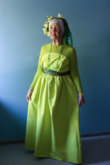 an elderly woman model in a green dress and a wreath, age 81	