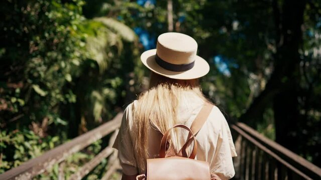 Romantic blonde woman tourist in straw hat walking to ocean sandy beach in sunny day, rear view. Female lady enjoying nature on vacations summer holidays. Travel, tourism, journey, rest relax concept.