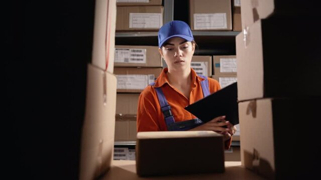 Female inventory manager checks stock and writing in the clipboard, searching parcel. Young woman working in a warehouse storeroom