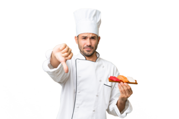 Young caucasian chef holding a sushi over isolated background showing thumb down with negative expression