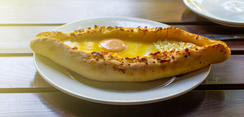 Adjara-style khachapuri, baked dough with egg, cheese and two pieces of butter on a white plate in a cafe.