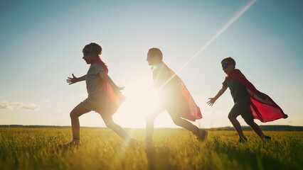 team superhero. a group of children are running across the field in a superhero costume with a silhouette of a red cape at sunset. the concept of a happy family childhood dream. teamwork superhero © maxximmm