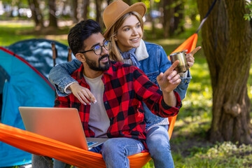 Young freelancer working on laptop in the forest, with his girlfriend next to him