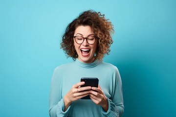 Portrait of a young woman with curly hair using mobile phone on blue background - obrazy, fototapety, plakaty