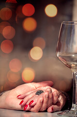 Young daughter holding old mother's hand. Close up of mom and daughter hands next to a wine glass and bokeh lights as background. Date with mom.