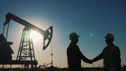 handshake business oil contract. handshake a worker and businessman shaking hands against backdrop of an oil pump sunlight. oil extraction business concept. silhouette handshake business contract - Powered by Adobe