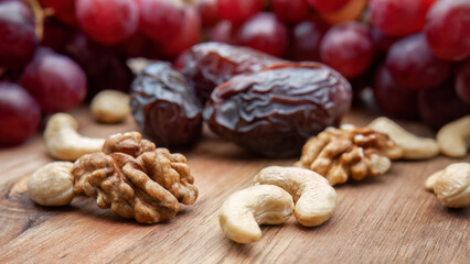 Walnuts and cashews close up against a background of large dates and red grapes. Horizontal. Selective focus.