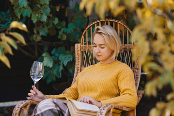 woman in sweater reads a book and drinking wine in terrace