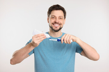 Happy man squeezing toothpaste from tube onto toothbrush on white background