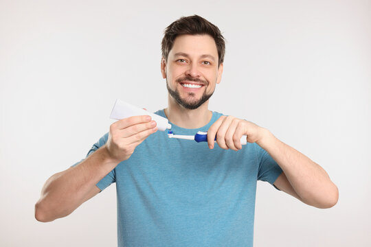 Happy man squeezing toothpaste from tube onto toothbrush on white background