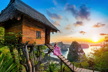 Young girl on steps of house on tree at sunrise in Nusa Penida island, Bali in Indonesia. - obrazy, fototapety, plakaty