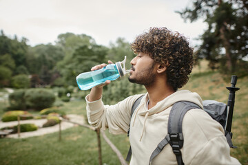 side view of indian traveler with backpack drinking water with landscape on background