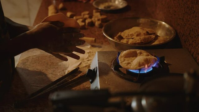 Cook sculpts and rolls wheat dough and cooks a traditional Indian dish chapati on an open fire on gas in the kitchen. Indian National Bread