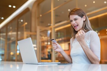 Young caucasian woman doing digital banking using her laptop and credit card online in a random cafe