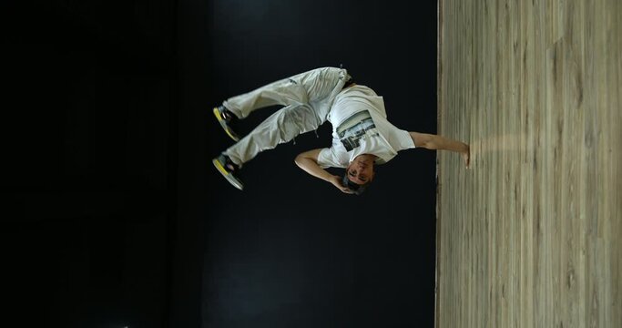 Vertical shot. Male breakdancer dancing on black background. Super slow motion