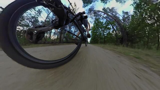 Cyclist pedals mountain bicycle, rear wheel view. Bicyclist rides MTB bike along sandy road in forest. Chain drive, rear derailleur with cassette. Gearshift. Jockey wheels. Low angle Fisheye lens