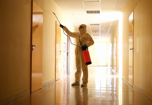 Person wearing white chemical protection suit holding spray bottle with disinfectant chemicals. Stop spread of highly contagious coronavirus or COVID-19 virus.