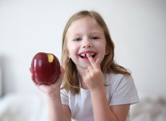 Portrait of joyful child girl without teeth holds apple. Change of milk teeth and hard food concept